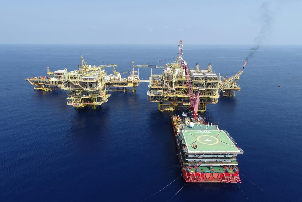 Aerial shot of multiple offshore oil platforms in a serene, blue sea under clear skies.